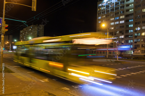 A blurry bus moves along the avenue in the evening.