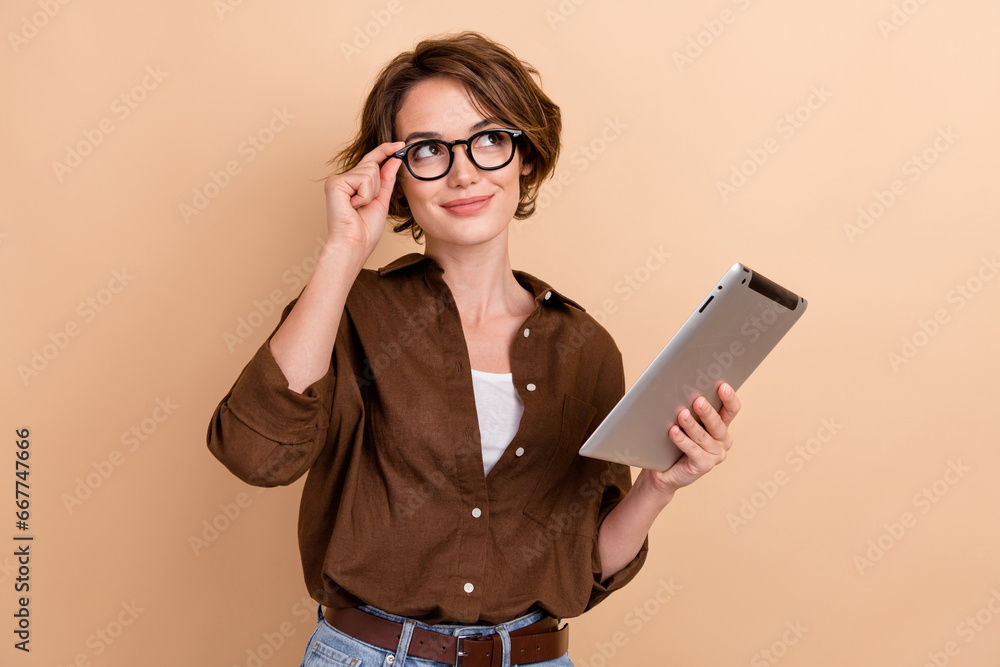 Photo of dreamy thoughtful girl dressed brown shirt eyewear texting modern gadget looking empty space isolated beige color background