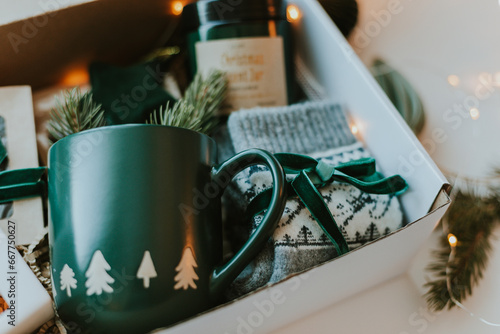 Close-up of Christmas gift box. Cozy mug for coffee, warm gray socks, aroma candle in jar. Christmas and Holiday Gift Ideas