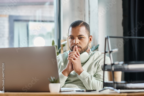 thoughtful young man looking seriously at his laptop with fingers near face, working process