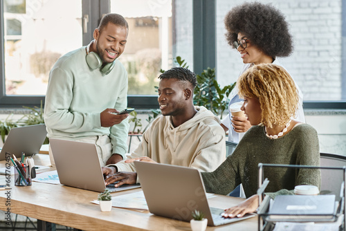 cheerful friends in casual bold outfits with coffee and phone in hands smiling happily, coworking