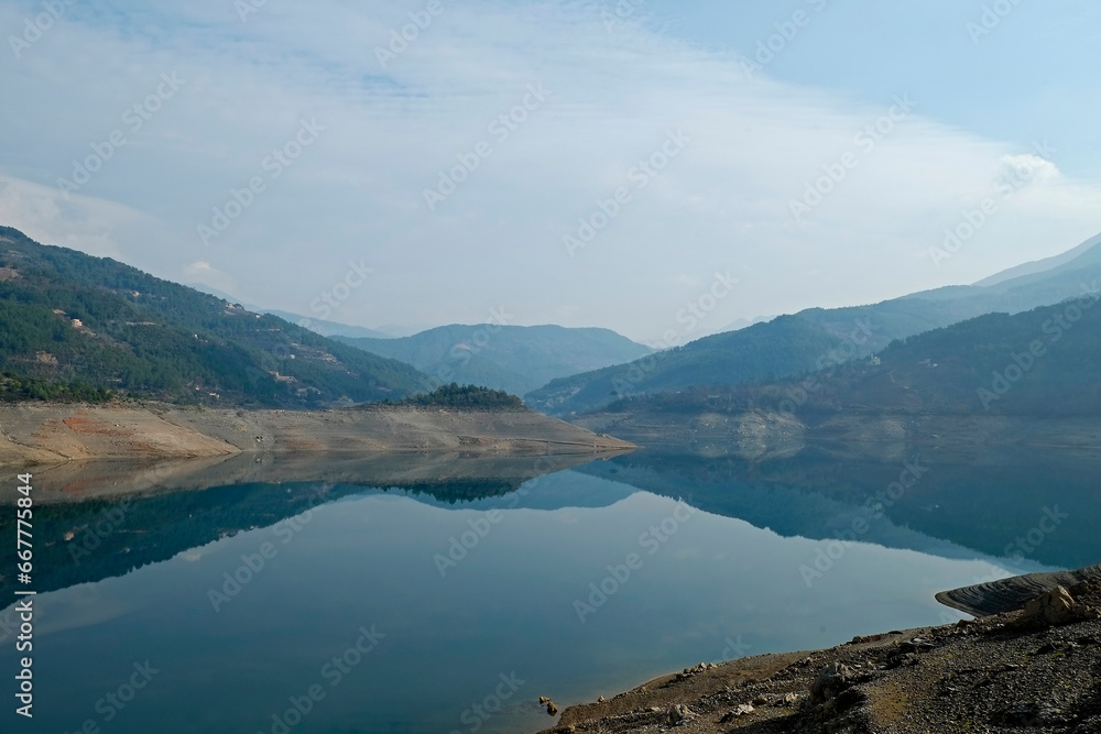 Beautiful view of mountain lake on a calm foggy day with gray cloudy skies. Copy space, background.