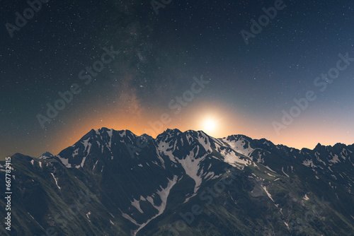 Beautiful night landscape, snow covered mountains in the night. Bright milky way galaxy behind them.