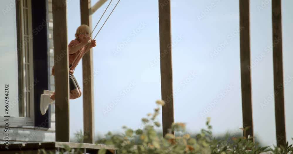 Caucasian kid boy swinging on a swing on over a porch of family house Caucasian kid boy swinging on a swing on over a porch of family house