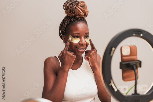 Print op canvas Young african american woman filming a beauty vlog applying patches under eyes i