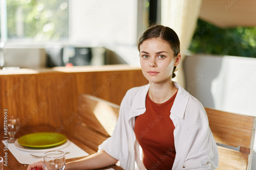 Stylish woman sitting at dining table drinking water from a glass, home modern interior, sunset light, lifestyle in comfort. Stylish woman sitting at dining table drinking water from a glass, home modern interior, sunset light, lifestyle in comfort.