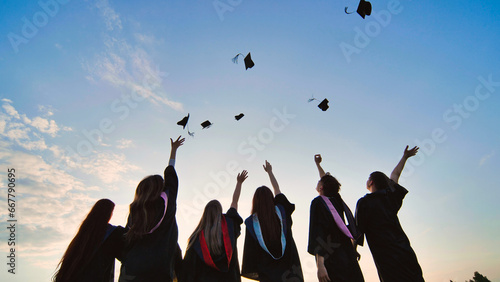 Silhouettes of graduates toss their caps at sunset.