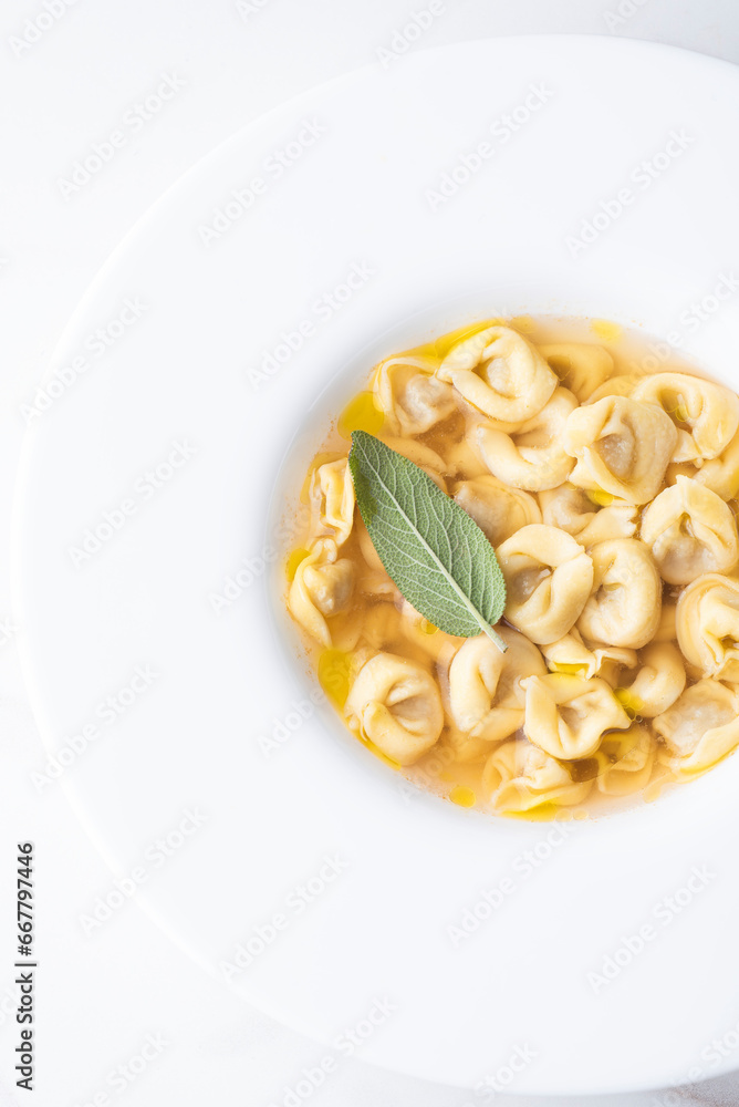 Italian ravioli with aromatic broth and sage leaf in a white plate. Close-up,  top view. Italian traditional winter and holiday cuisine