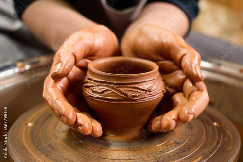 Pottery wheel. Artisan's creation. Dirty form. Handicraft skill. Clay work. Potter's hands gently and surely formed by clay pot on potter's wheel.