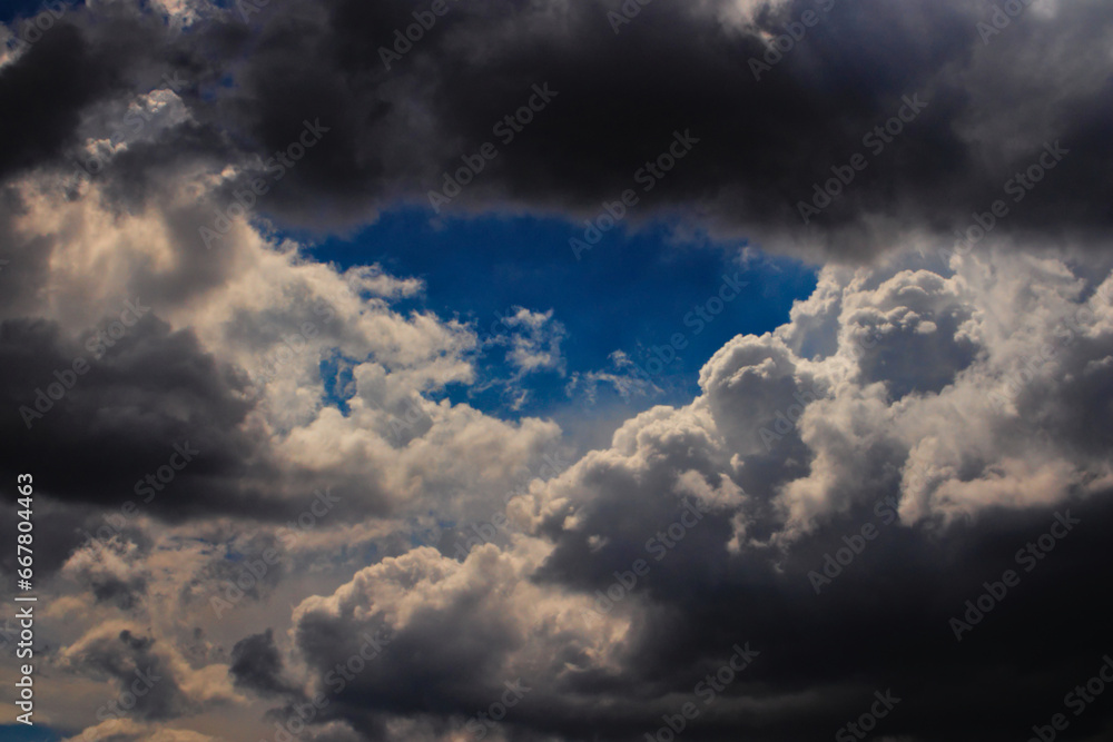 Fototapeta premium patch of blue sky, framed by shadowy cumulus clouds.