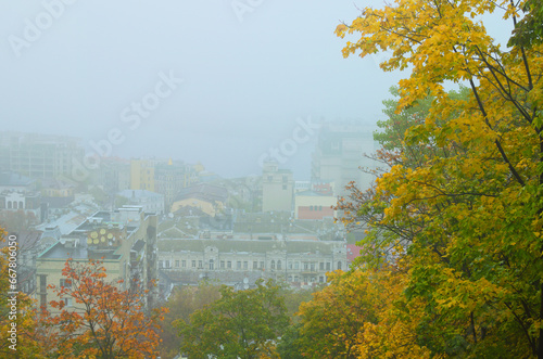 Picturesque aerial landscape view of ancient Podil neighborhood during fog. Mysterious cityscape. Kyiv during autumn thick fog. Tree leaves boarder, natural composition