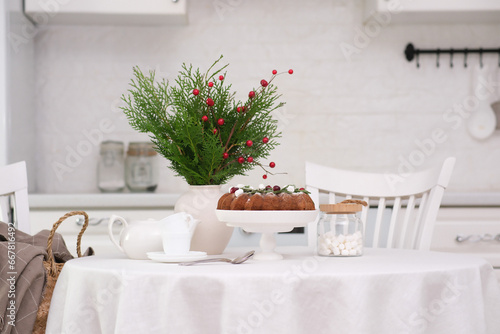 Christmas home interior in white kitchen-Christmas chocolate bundt cake with fresh berries and rosemary. Winter baking at Christmas. Ceramic vase with spruces brunches.. © Di_Ilikaeva