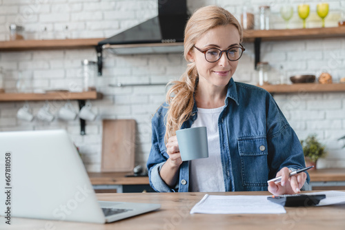 Paying bills, funds calculation on laptop at home. Mature woman counting money at home kitchen, mortgage, loan, having debt. Internet banking concept photo