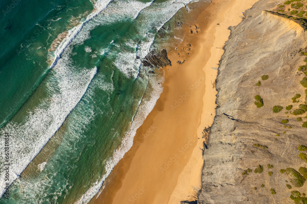 Sandy beach and dramatic cliffs on Atlantic Ocean coastline in Portugal. Aerial drone view
