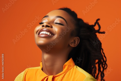 A cheerful African woman wearing makeup, her eyes closed as she smiles with satisfaction. orange studio background