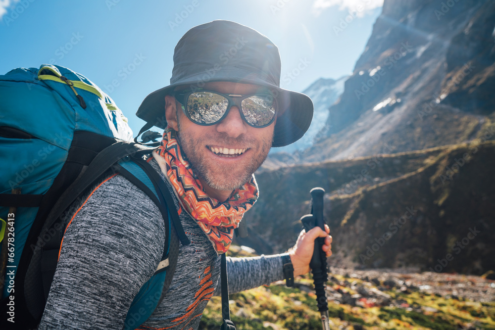 Portrait Young hiker backpacker man in sunglasses smiling at camera in Makalu Barun Park route during high altitude acclimatization walk. Mera peak trekking route, Nepal. Active vacation concept image - obrazy, fototapety, plakaty 