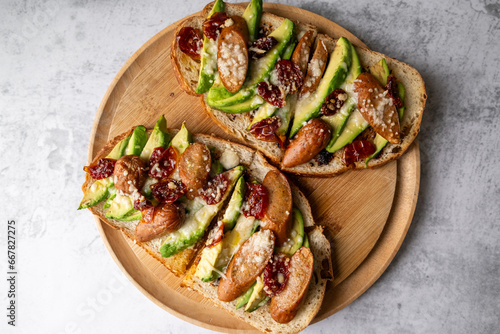 Avocado sourdough bread toast with sausage and sun-dried tomato on wooden plate. Healthy food concept.