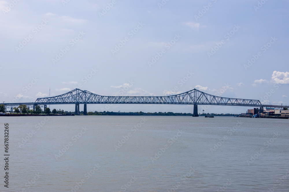 a gorgeous summer landscape along the Mississippi River with the Crescent City Connection bridge over the water with blue sky and clouds at sunset in New Orleans Louisiana USA