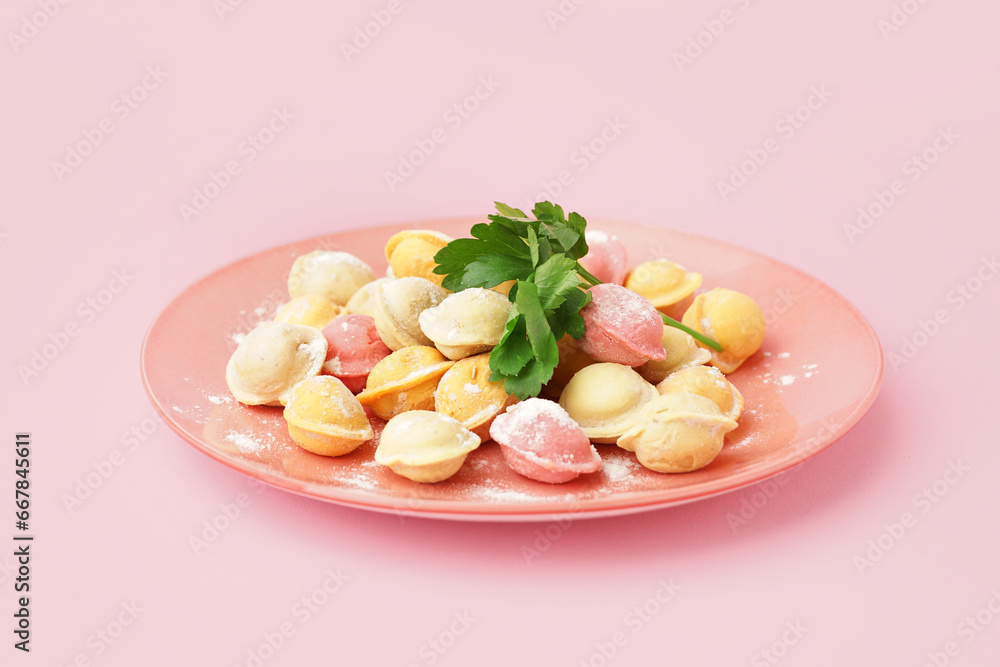 Plate with colorful raw dumplings and parsley on pink background Plate with colorful raw dumplings and parsley on pink background