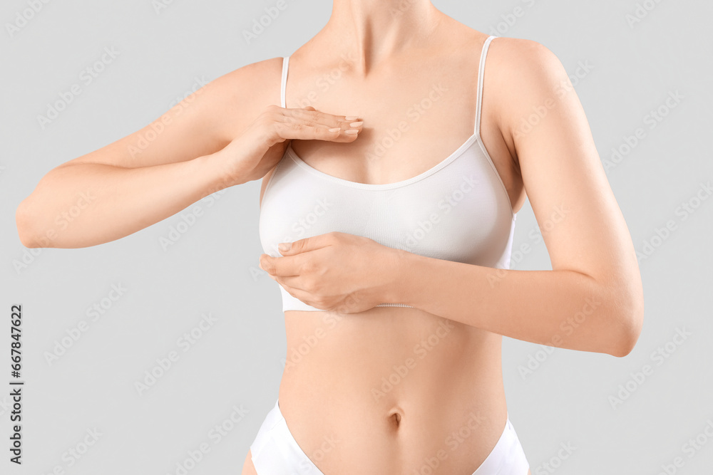 Young woman touching her breast on grey background