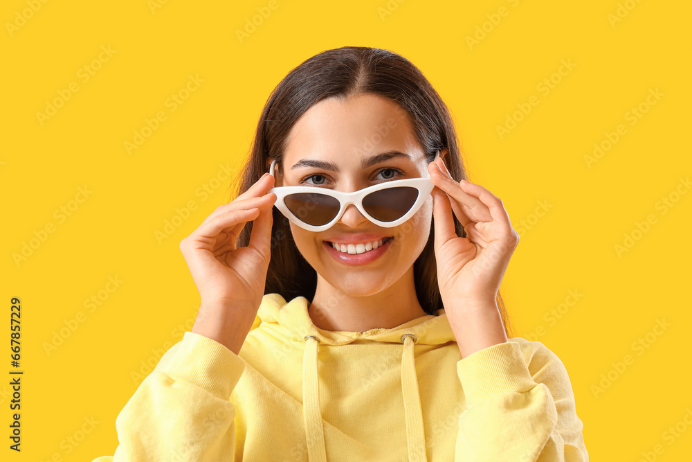 Young woman in sunglasses and hoodie on yellow background, closeup Young woman in sunglasses and hoodie on yellow background, closeup