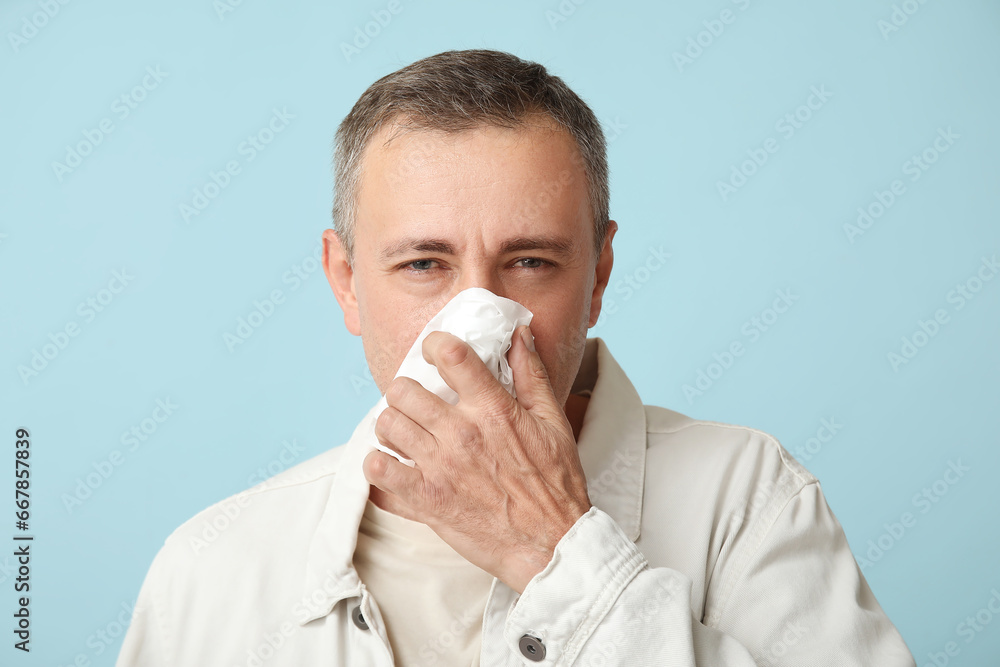 Ill mature man with tissue blowing nose on blue background Ill mature man with tissue blowing nose on blue background