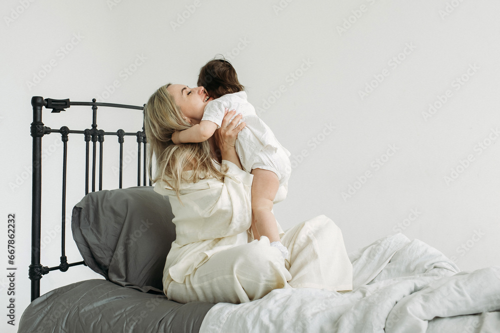 Portrait of a little girl and mother sitting on the bed in the morning after sleep. Happy mother hugs her child, smiles. Portrait of a little girl and mother sitting on the bed in the morning after sleep. Happy mother hugs her child, smiles.