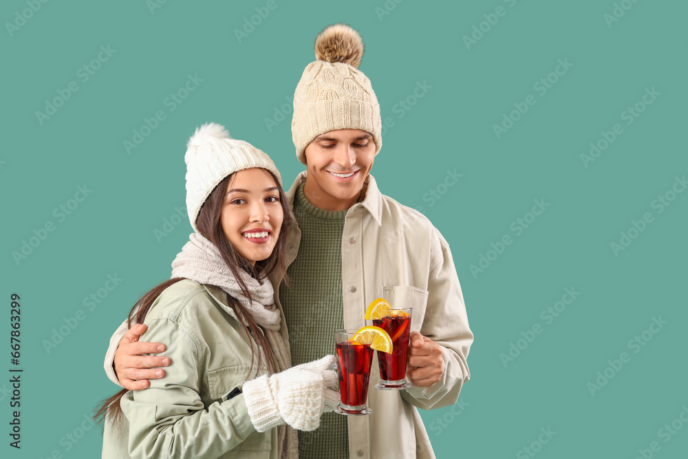 Happy couple in warm clothes with glasses of tasty mulled wine on turquoise background Happy couple in warm clothes with glasses of tasty mulled wine on turquoise background
