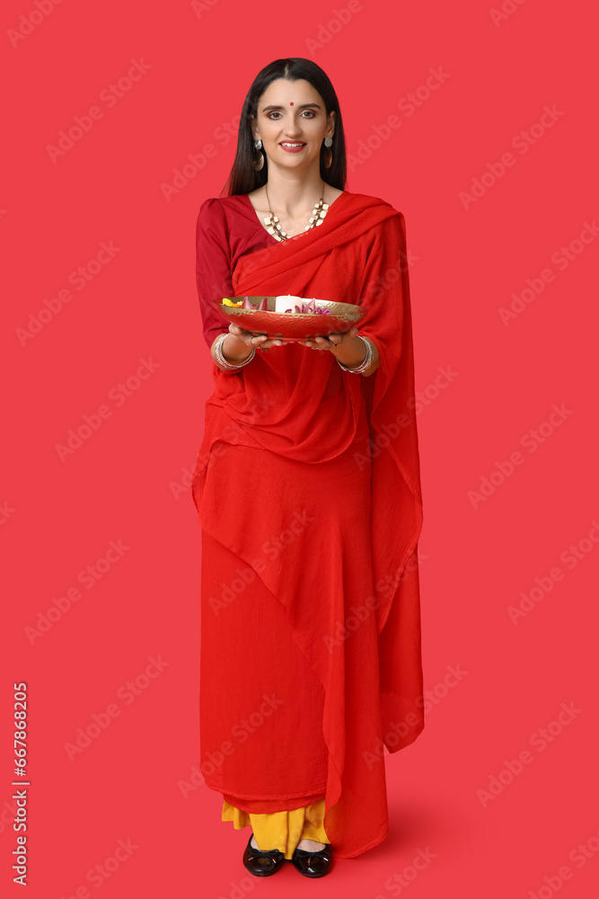 Beautiful young Indian woman in sari with candle and flowers on red background. Divaly celebration Beautiful young Indian woman in sari with candle and flowers on red background. Divaly celebration