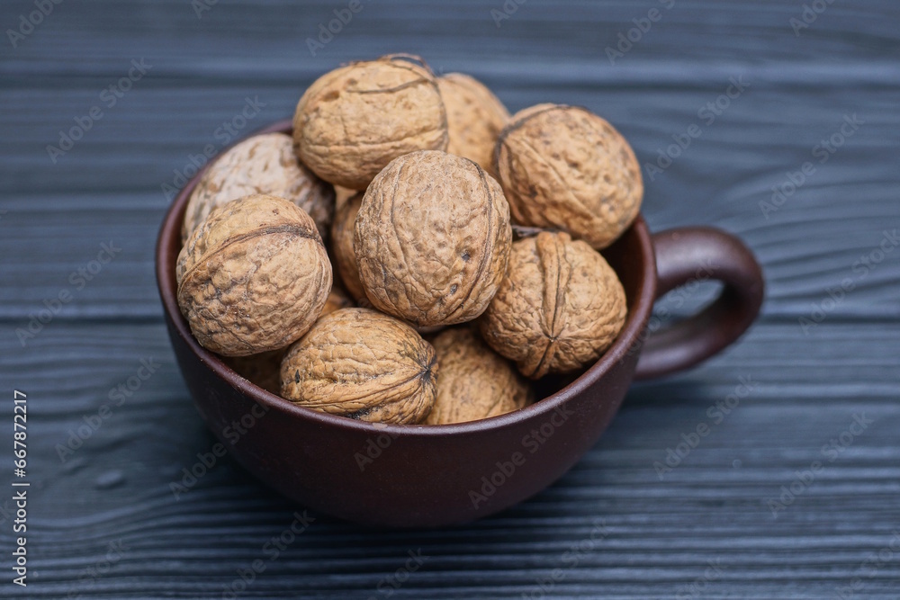 a bunch of walnuts in a brown ceramic cup stands on a black wooden table a bunch of walnuts in a brown ceramic cup stands on a black wooden table