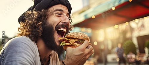 Young man eating burger outdoors close up Street food being enjoyed by bearded man photo