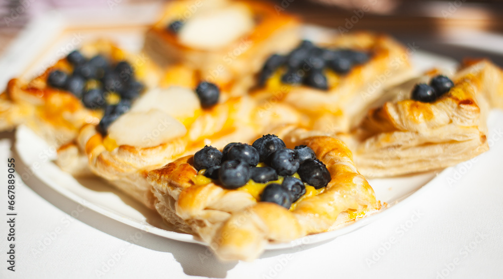 Closeup of a puff homemade tasty pastry filled with yellow cream, blueberries and peaches on a white plate, side view Closeup of a puff homemade tasty pastry filled with yellow cream, blueberries and peaches on a white plate, side view