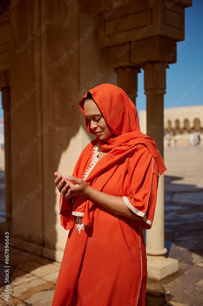 Young Arabic Muslim woman praying, making Islamic pray dua with cupped hands standing near marble columns at mosque Young Arabic Muslim woman praying, making Islamic pray dua with cupped hands standing near marble columns at mosque
