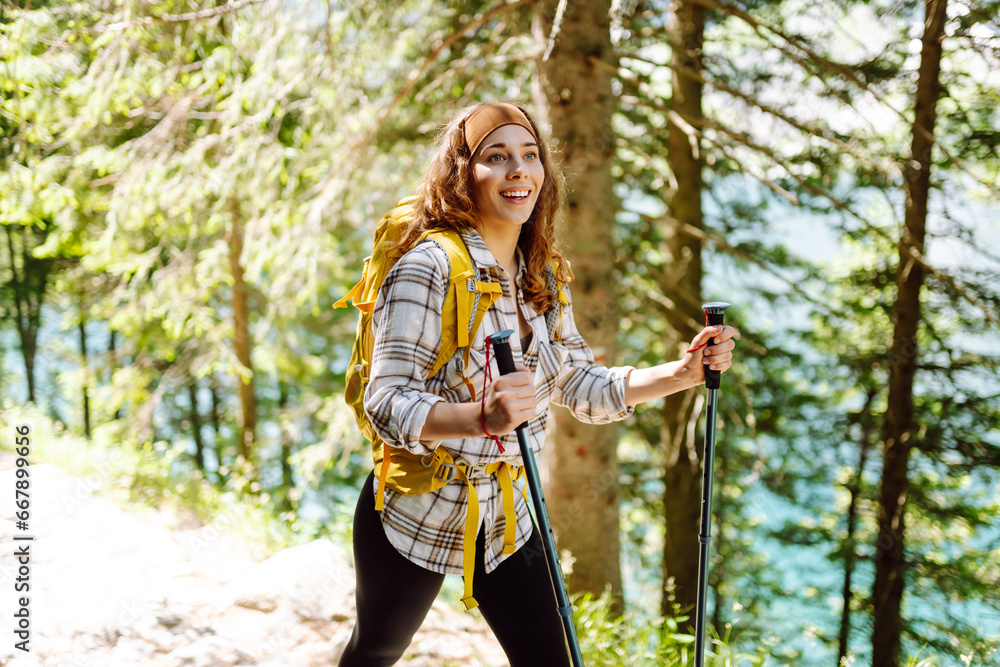 Beautiful woman with a yellow backpack enjoys hiking on a mountain trail along a lake. Active lifestyle.