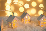 Wooden houses garland string lights on snow and glowing lights bokeh background. Christmas, New Year greeting card with copy space. Holiday illumination, home decor.