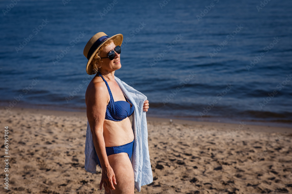 An old woman in a straw hat, sunglasses and a swimsuit is resting on the beach. An old woman in a straw hat, sunglasses and a swimsuit is resting on the beach.
