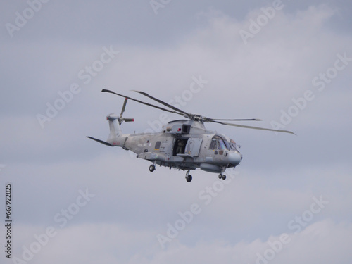 Ein grauer Hubschrauber der englischen Küstenwache fliegt mit geöffneter Tür am Himmel vor der englischen Küste bei Falmouth England