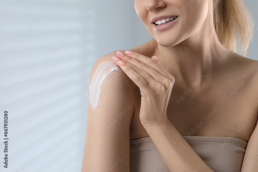 Woman applying body cream onto shoulder on light grey background, closeup. Space for text Woman applying body cream onto shoulder on light grey background, closeup. Space for text