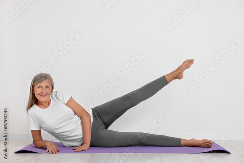 Happy senior woman practicing yoga on mat near white wall