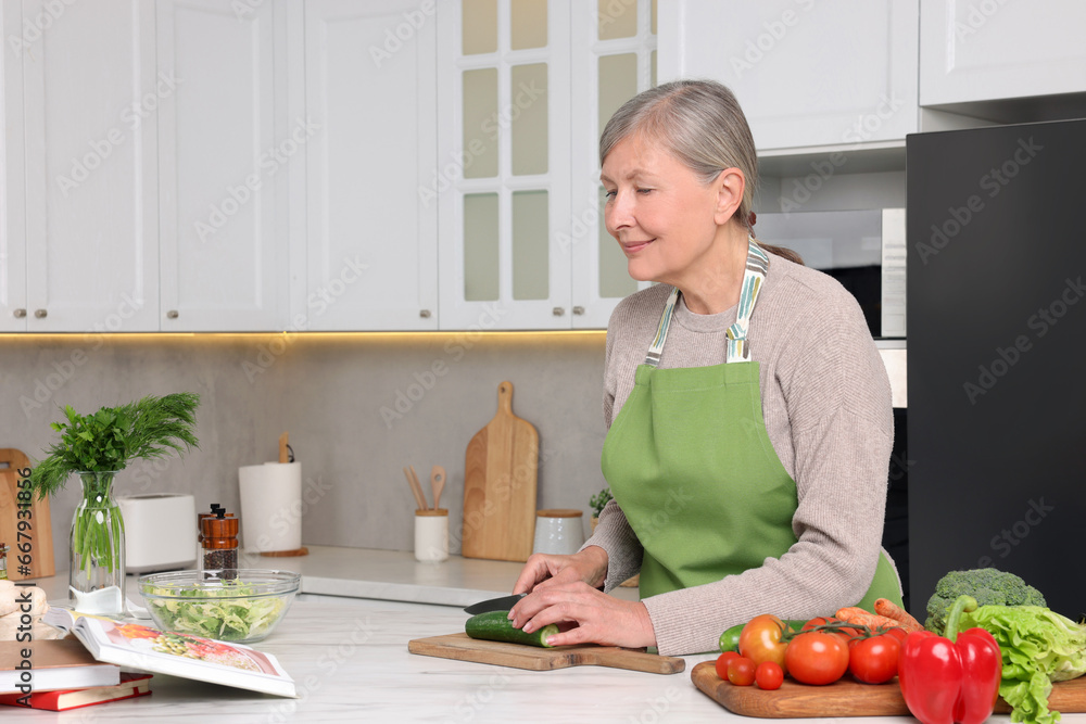 Senior woman cooking by recipe book in kitchen