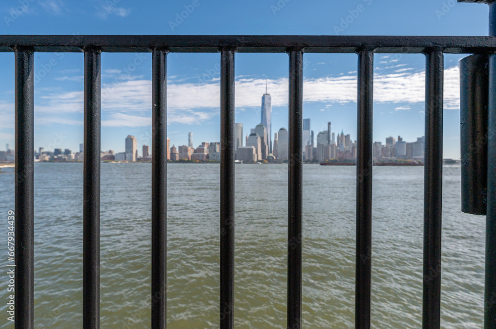 New York City skyline in the background, framed by a foreground railing. Perfect for capturing urban vistas with architectural detail. New York City skyline in the background, framed by a foreground railing. Perfect for capturing urban vistas with architectural detail.