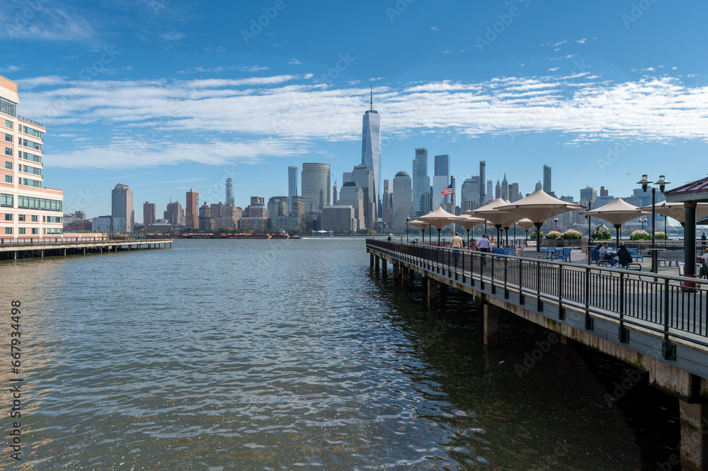 Stunning NYC skyline unfolds from Jersey City Harbour, with iconic skyscrapers reaching for clear skies. The Hudson River reflects the architectural marvels, epitomizing urban beauty across the waters