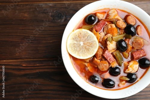 Meat solyanka soup with sausages, olives and vegetables on wooden table, top view. Space for text