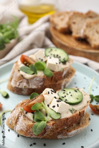 Tasty vegan sandwiches with tofu, cucumber, tomato and sesame seeds on table, closeup