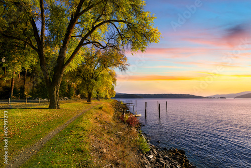 Fototapeta Naklejka Na Ścianę i Meble -  Autumn sunset view with fall colors on the leaves along the tree lined Centennial Trail path as it makes it's way along the lake near Silver Beach in Coeur d'Alene, Idaho USA.