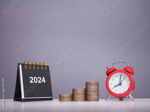 2024 desk calendar, Red alarm with stack of coins. The concept of saving money, Financial, Investment and Business growing in new year 2024. photo