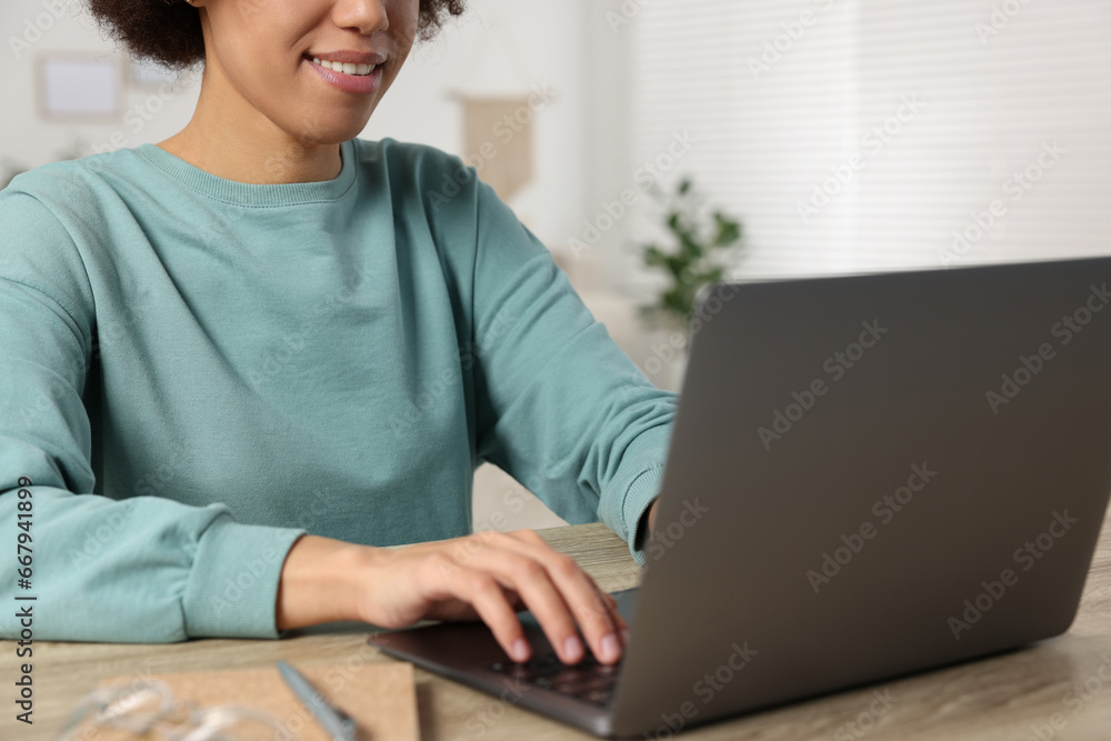 Young woman using laptop at wooden desk in room, closeup Young woman using laptop at wooden desk in room, closeup