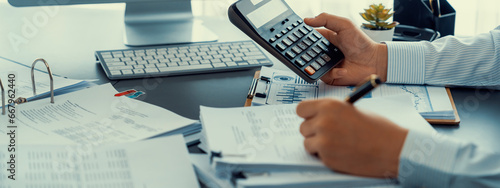 Corporate auditor calculating budget with calculator on his office desk. Dedicated accountant professional of accounting business company analyzing financial document to forecast income. Insight photo