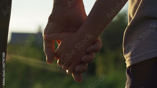 The clasped hands of an older man and a little boy in the sunset light