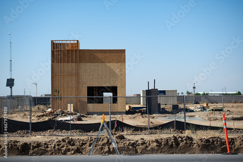 A fenced-off construction site has the ground cleared, and a fast food location rises up, built out of wood framing and plywood. Located in the San Joaquin Valley, it highlights development there.